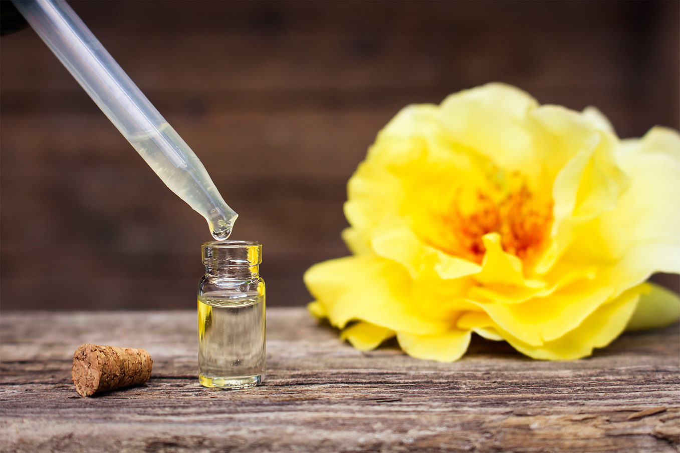 Bottles of essential oil and roses on old wooden background.